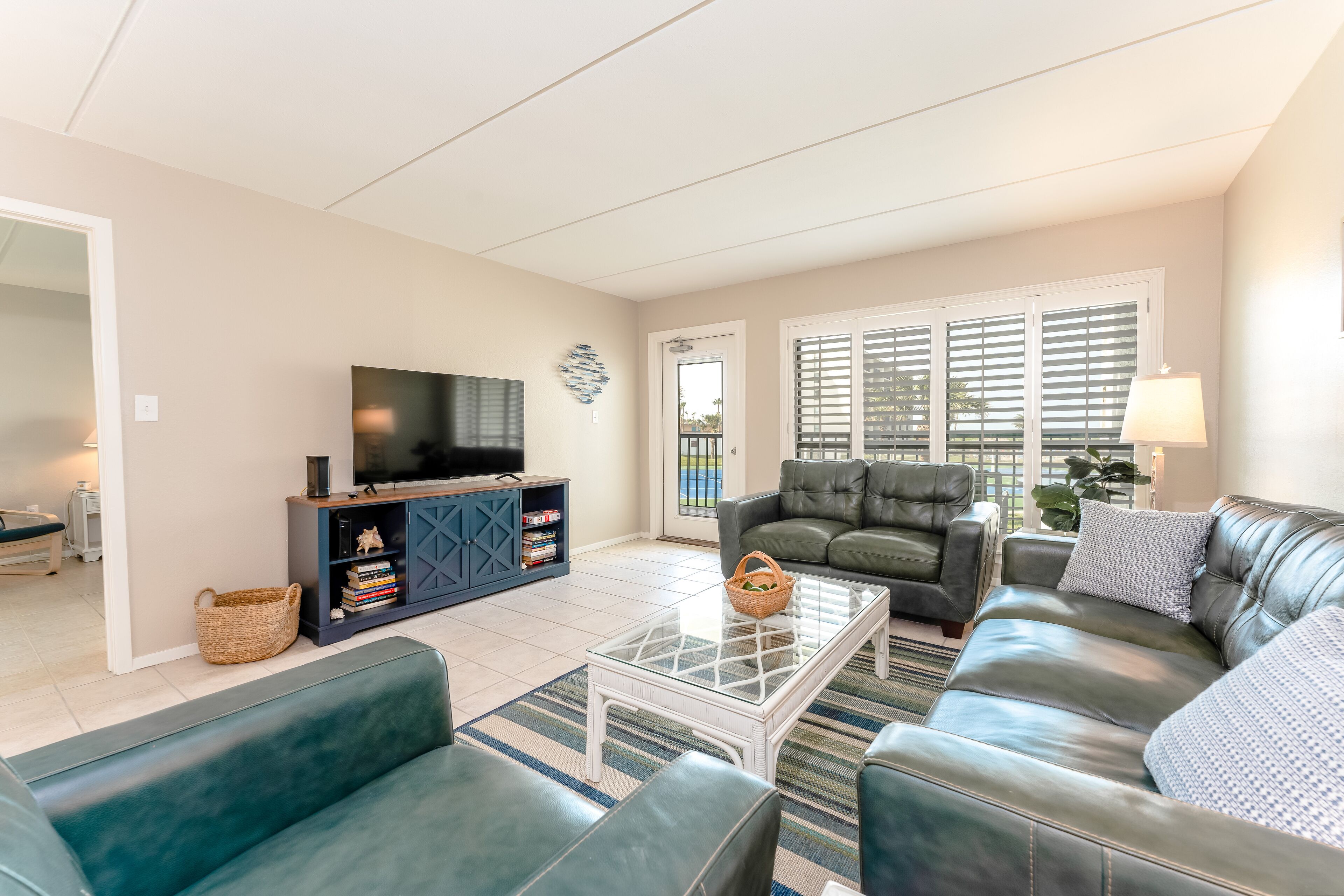 A living room with a sofa set, a glass coffee table, a TV on a cabinet, and a view through the window.