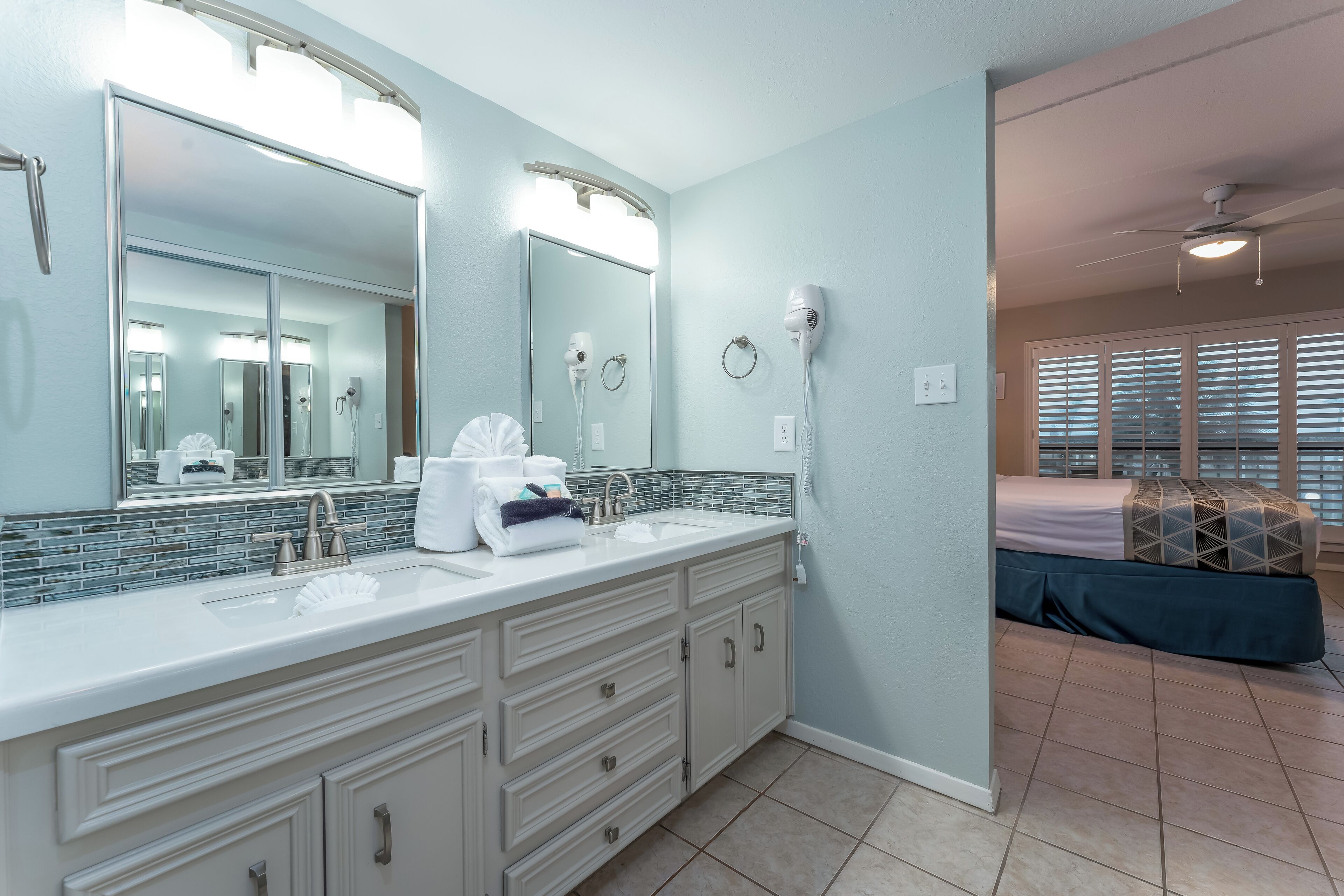 A bathroom with a large mirror, two sinks, a towel rack, and a hairdryer.