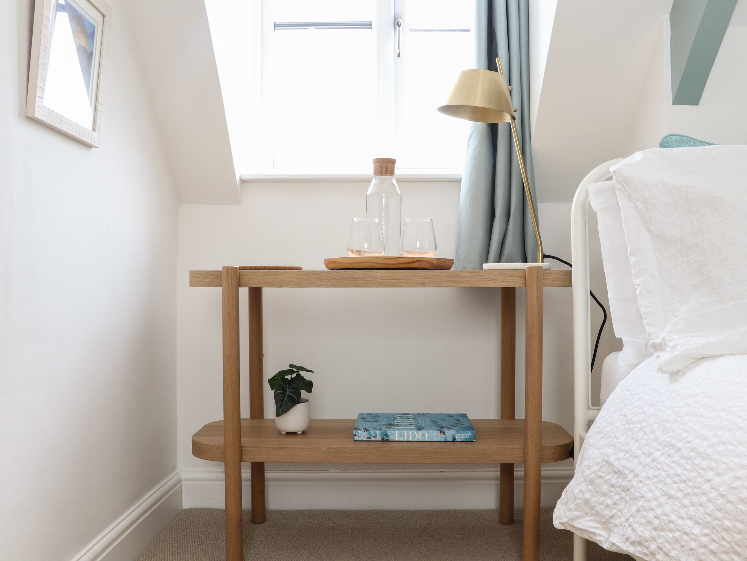 Une table de chevet en bois avec une plante, un livre et un ensemble de verres.