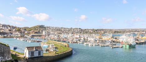 A harbor with boats docked, a small building on the shore, and a town in the background.