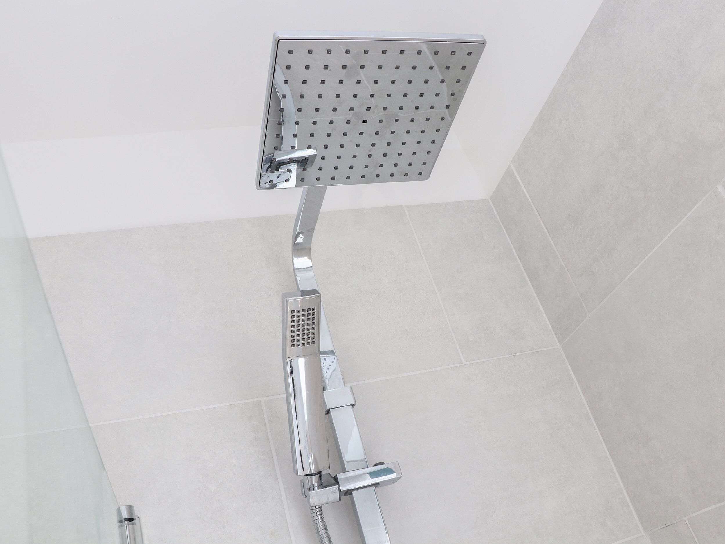 Een douche met een vierkante douchekop en een handdouche.