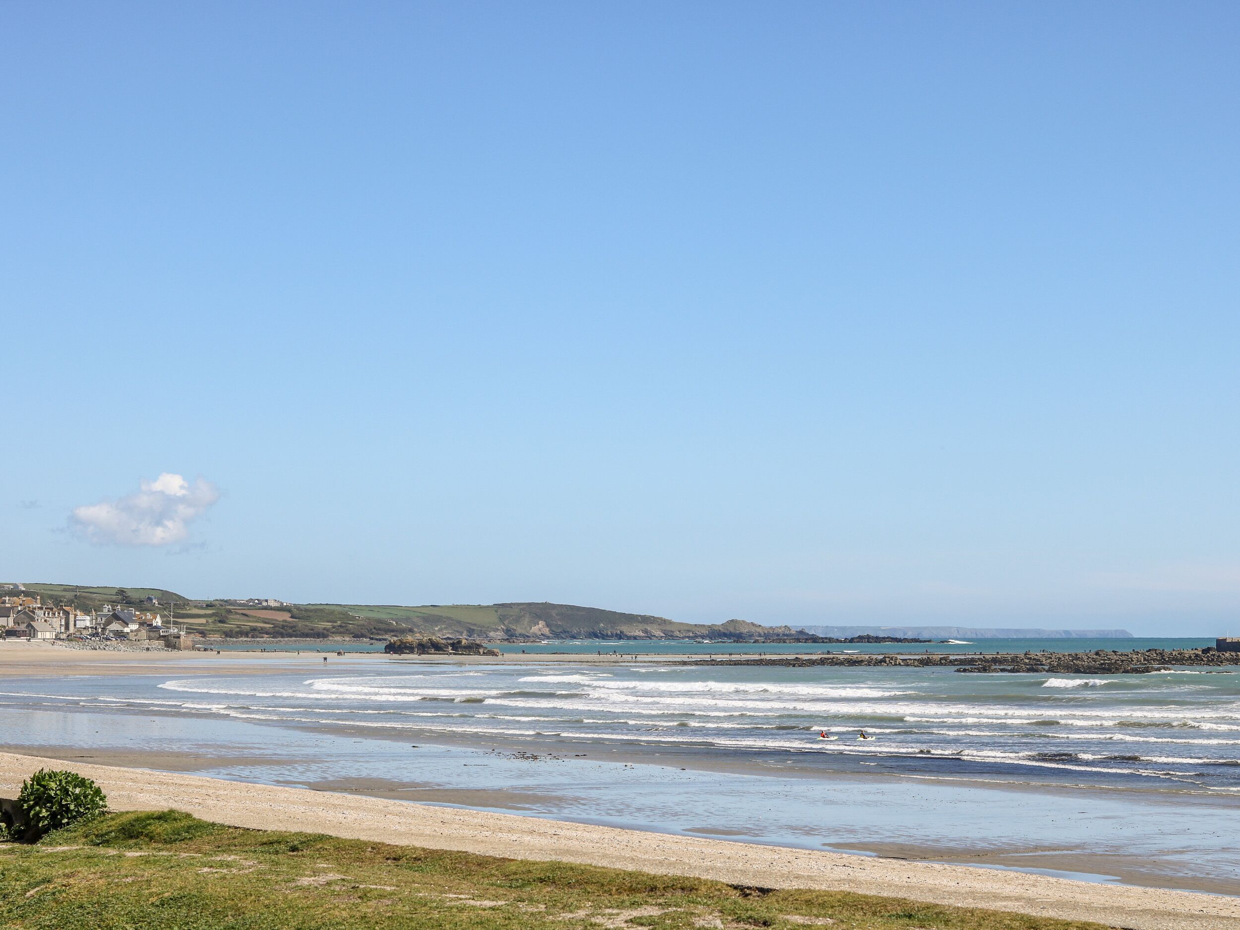 Une plage côtière, avec un ciel dégagé, des vagues et une ville qui se dessine à l’horizon.