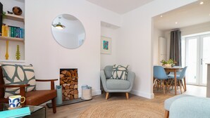 Ein modernes Wohnzimmer mit Kamin, einem runden Spiegel und einem Essbereich mit blauen Stühlen.