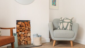 Ein Wohnzimmer mit Kamin, einem runden Spiegel, einem gerahmten abstrakten Gemälde, einem grauen Sessel mit gemustertem Kissen und einem Teppich.
