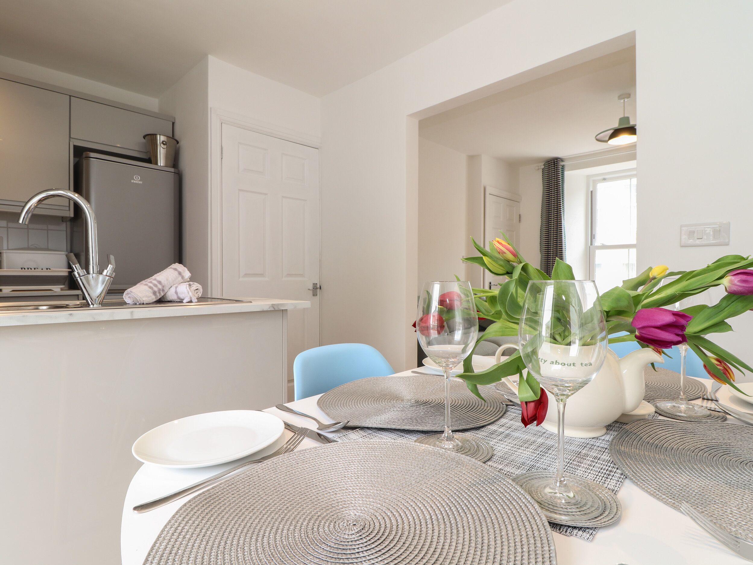 Un coin repas avec une table dressée pour deux personnes, comprenant des assiettes, des couverts et un vase avec des fleurs.