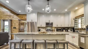 A modern kitchen with white cabinets, stainless steel appliances, and a central island with bar stools. - Alpine Splash,  Private indoor pool, theater/gaming, Pond, Basketball court!!! (Sevierville)