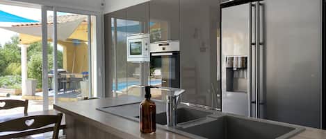 A modern kitchen with a stainless steel refrigerator, a built-in oven, and a large window overlooking a pool.