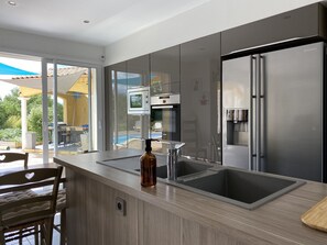 Una cocina moderna con un refrigerador de acero inoxidable, un horno empotrado y un amplio ventanal con vistas a una piscina.