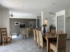 A modern kitchen with built-in appliances, a dining area with wicker chairs, and a large vase of flowers.