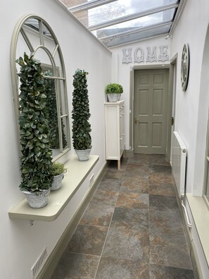 Enter a serene hallway with a glass ceiling, white door, and lush potted plants.