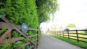 En landvej der fører hen til en gård med et træhegn og et skilt med teksten 'Little Glades Moss Farm'.