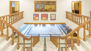 A grand staircase with wooden railings leading to a spacious area with artwork on the walls. - Olive County Manali (Manali)