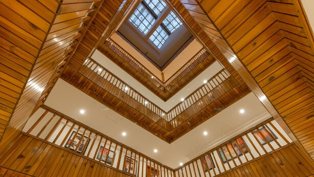 A multi-level wooden interior with a central skylight and balconies. - Olive County Manali (Manali)