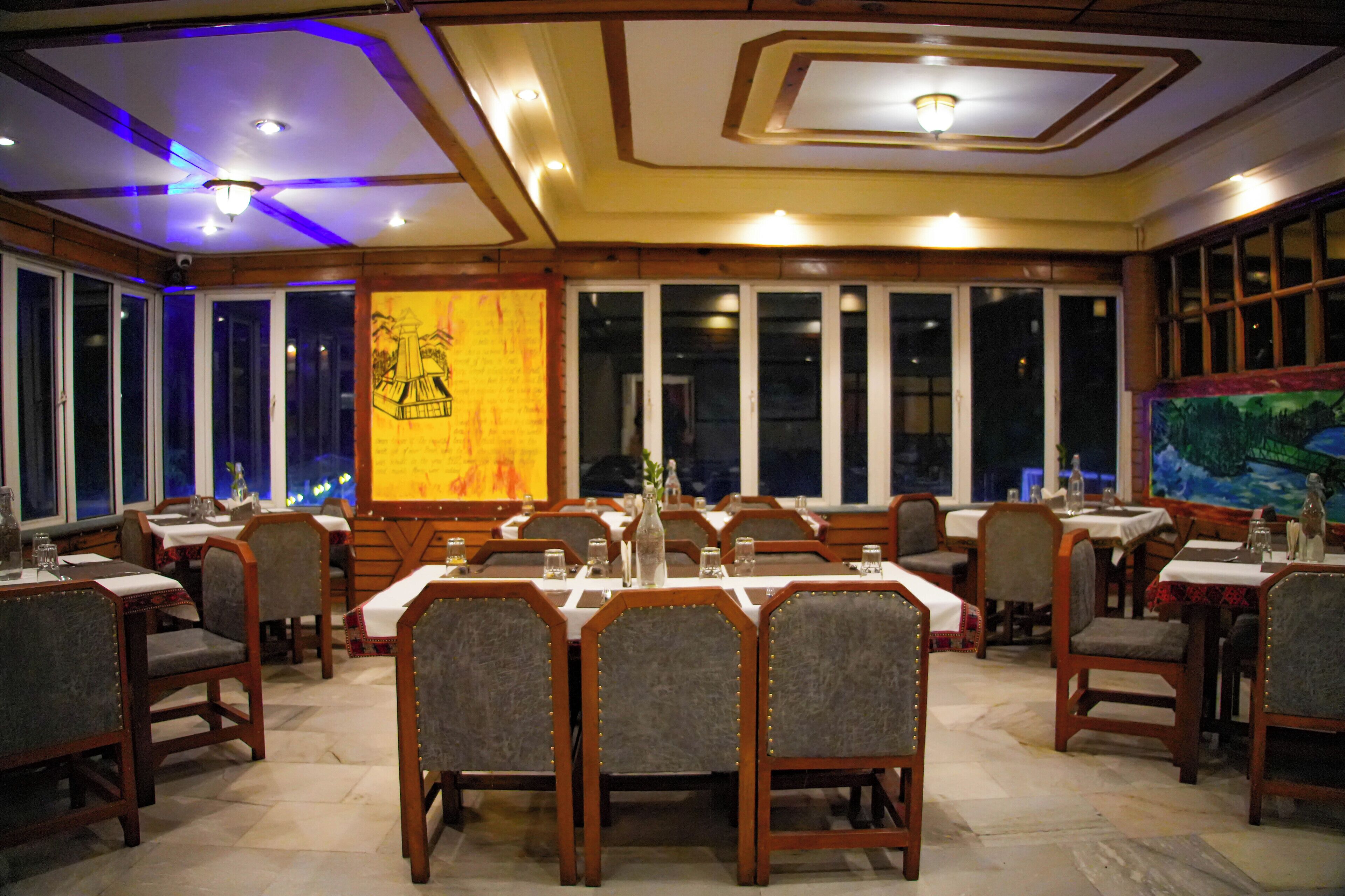 A restaurant with multiple tables and chairs, large windows, and a mural on the wall.
