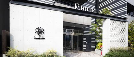 A modern hotel entrance with a glass door, a logo, and a name sign.