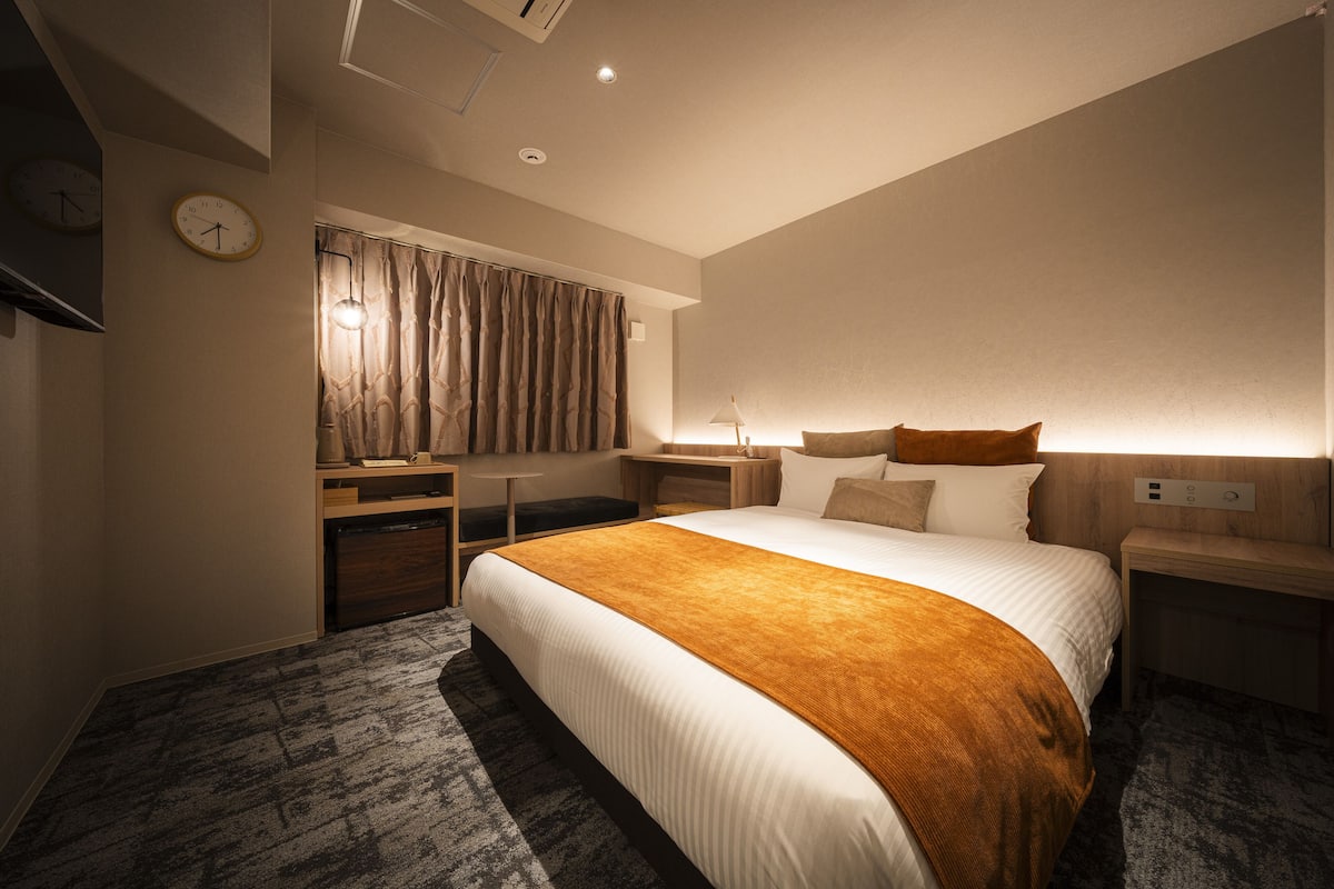 Una habitación de hotel con una cama grande, mesitas de noche, un escritorio y una ventana con cortinas.