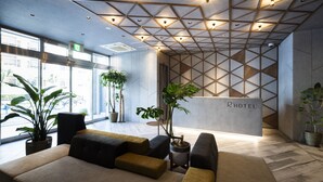 En moderne hotellobby med et geometrisk loftsdesign, behagelige siddeområder og store vinduer med udsigt udad.