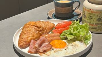 A plate with a croissant, ham, egg, and vegetables, a cup of coffee, and a mustard container.