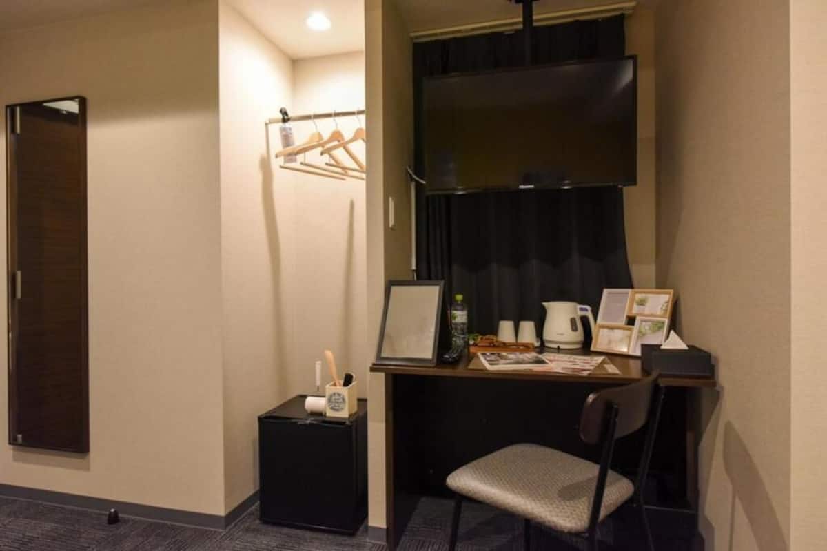 Habitación de hotel con escritorio, silla y mesita auxiliar con tetera y tazas.