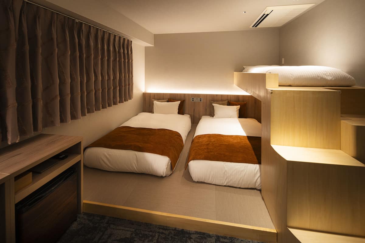 Habitación de hotel compacta con dos camas, un escritorio de madera y estantería empotrada.