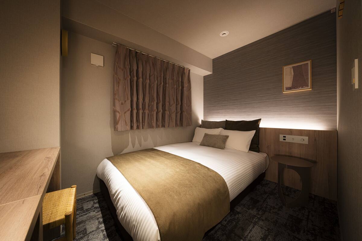 Una habitación de hotel moderna con una cama grande, un escritorio de madera y un taburete pequeño.