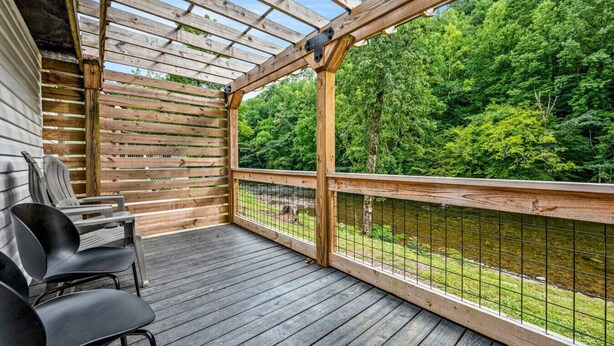 Eine Holzterrasse mit einer Pergola, Stühlen und Blick auf einen bewaldeten Bereich.