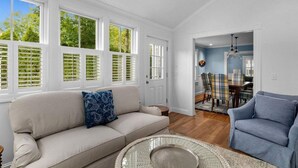 A spacious living room with a beige sofa, a blue armchair, and a dining area with plaid chairs. - Stroll Chatham's Historic Downtown / Shops, Dining, Galleries, Etc. (Chatham)
