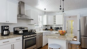 A modern kitchen with white cabinetry, stainless steel appliances, a central island with stools, and a visible door leading to another room. - Stroll Chatham's Historic Downtown / Shops, Dining, Galleries, Etc. (Chatham)
