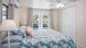A bedroom with a bed, a ceiling fan, an air conditioning unit, a window with curtains, and a view of the outdoors. - Captain's Quarters 3bed/2bath mobile home with dockage (Marathon)
