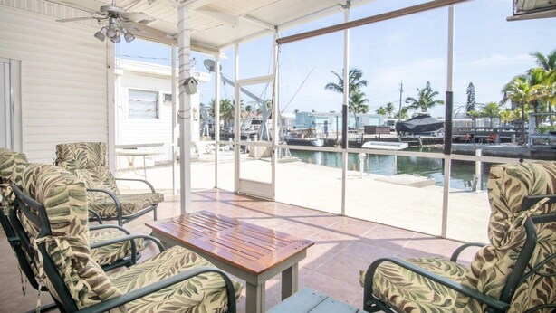 A covered outdoor seating area with chairs and a table, overlooking a marina with boats and palm trees. - Captain's Quarters 3bed/2bath mobile home with dockage (Marathon)