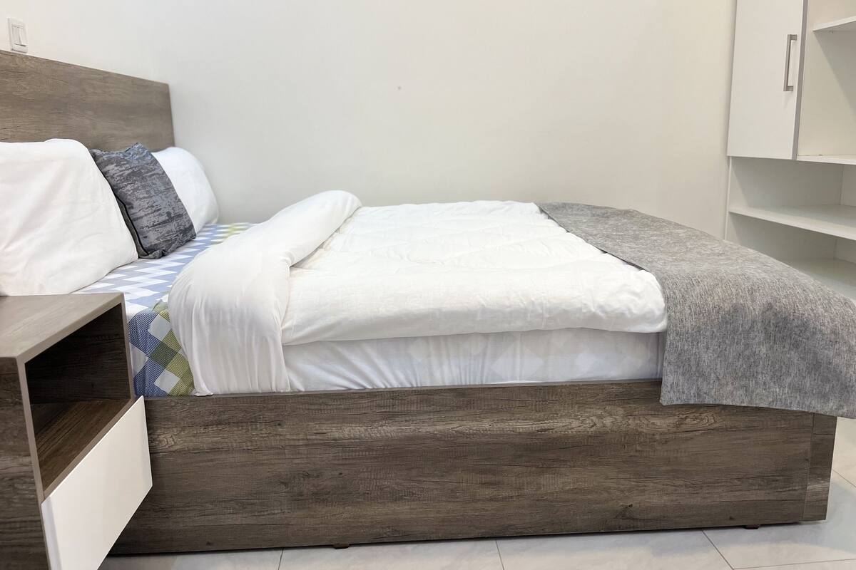 A bed with a wooden frame, white bedding, and a gray throw blanket.