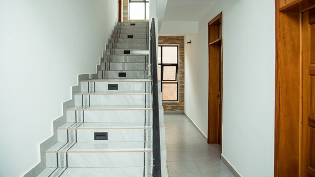 A modern staircase with a marble finish and a wooden door at the bottom. -  JLD Apartments (Kigali)