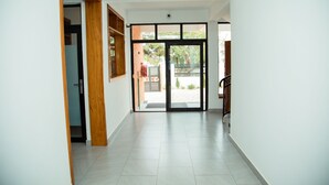 A hallway with a wooden door, a glass door leading outside, and a tiled floor. -  JLD Apartments (Kigali)