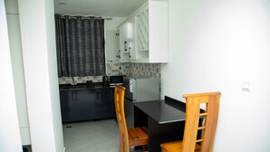 A compact kitchen with a black countertop, two wooden chairs, a refrigerator, and a microwave. -  JLD Apartments (Kigali)