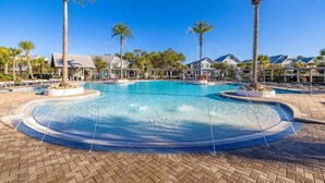 A swimming pool with palm trees, lounge chairs, and houses in the background.