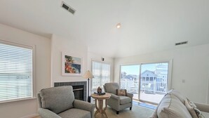A living room with a fireplace, two armchairs, a sofa, a small table, and a balcony with a view of buildings.