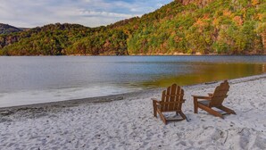 A beach with two wooden chairs facing a lake, surrounded by a forested hillside.