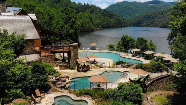 A resort with multiple swimming pools, a hot tub, and a wooden deck overlooking a lake.