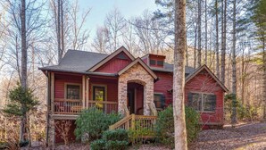 A two-story house with a stone chimney, a wooden porch, and a red exterior.