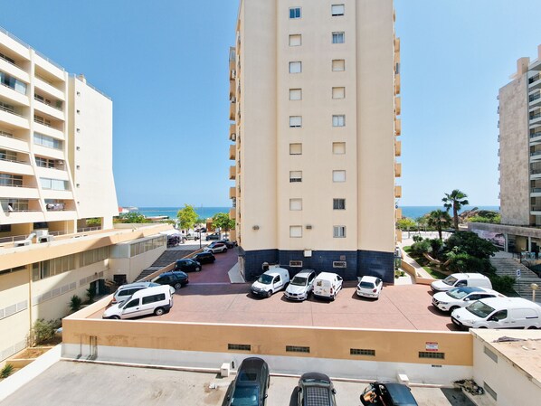 Un parking à étages abritant plusieurs voitures, entouré d’immeubles dotés de balcons donnant sur une zone côtière.