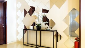 Um hall com parede estampada em padrão geométrico, mesa de console com objetos decorativos e um extintor de incêndio.