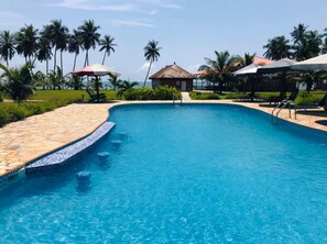 Une piscine d’un bleu éclatant, bordée de pierres, entourée de palmiers et de chaises longues.