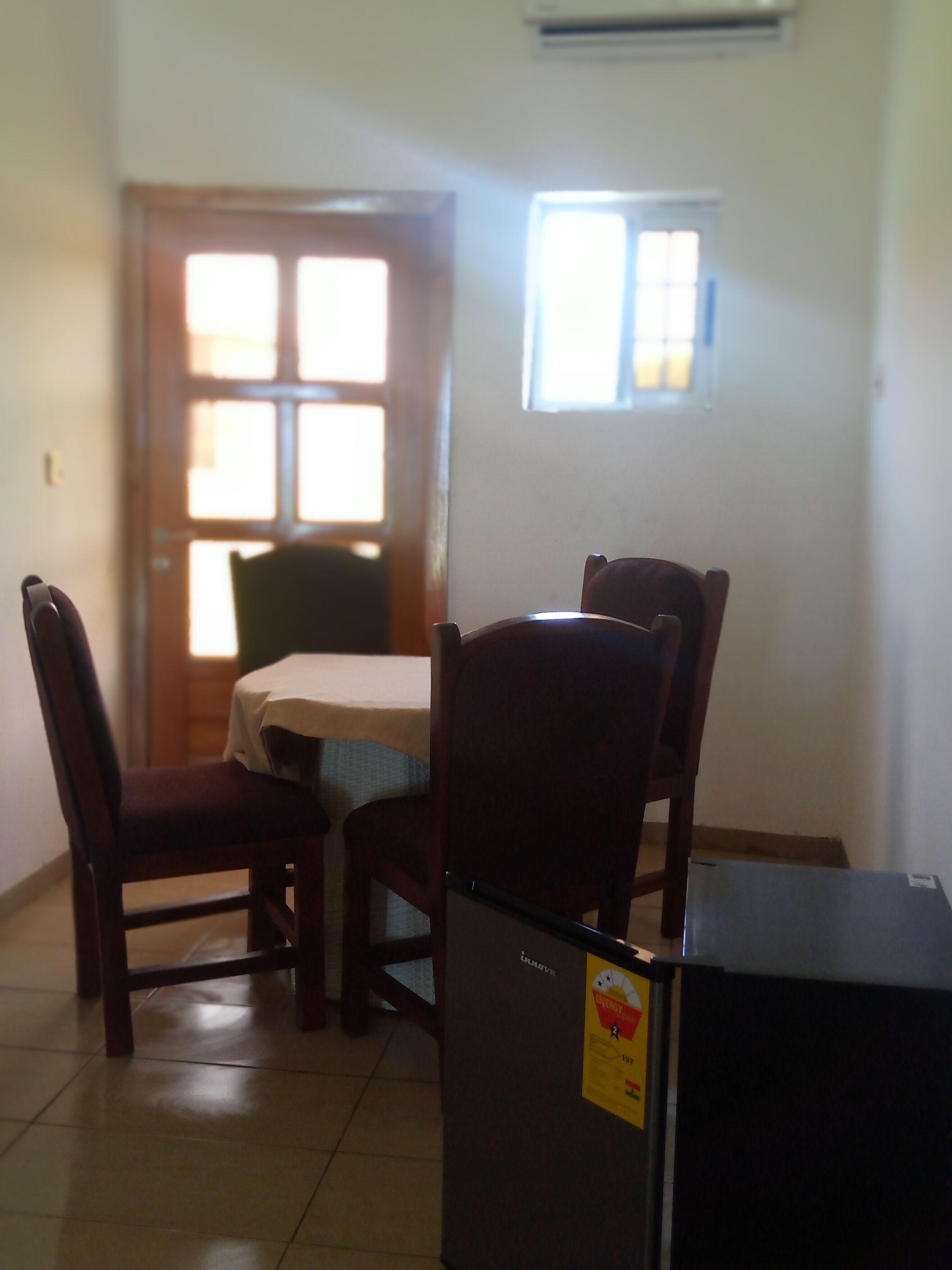 A dining area with a table and four chairs, a refrigerator, and a door with windows.