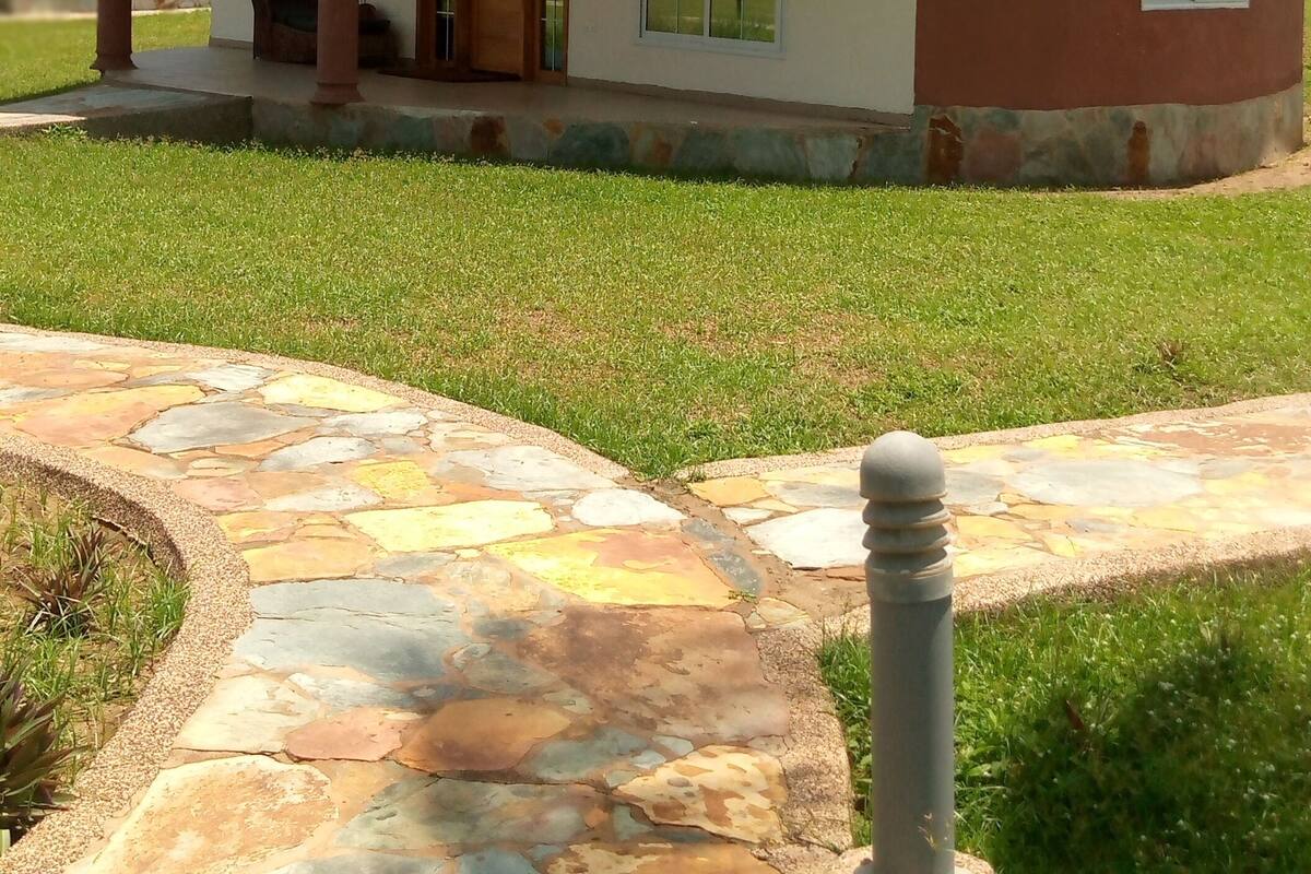 A single-story house with a brown roof and beige walls, a front porch, and a stone pathway leading to the entrance.