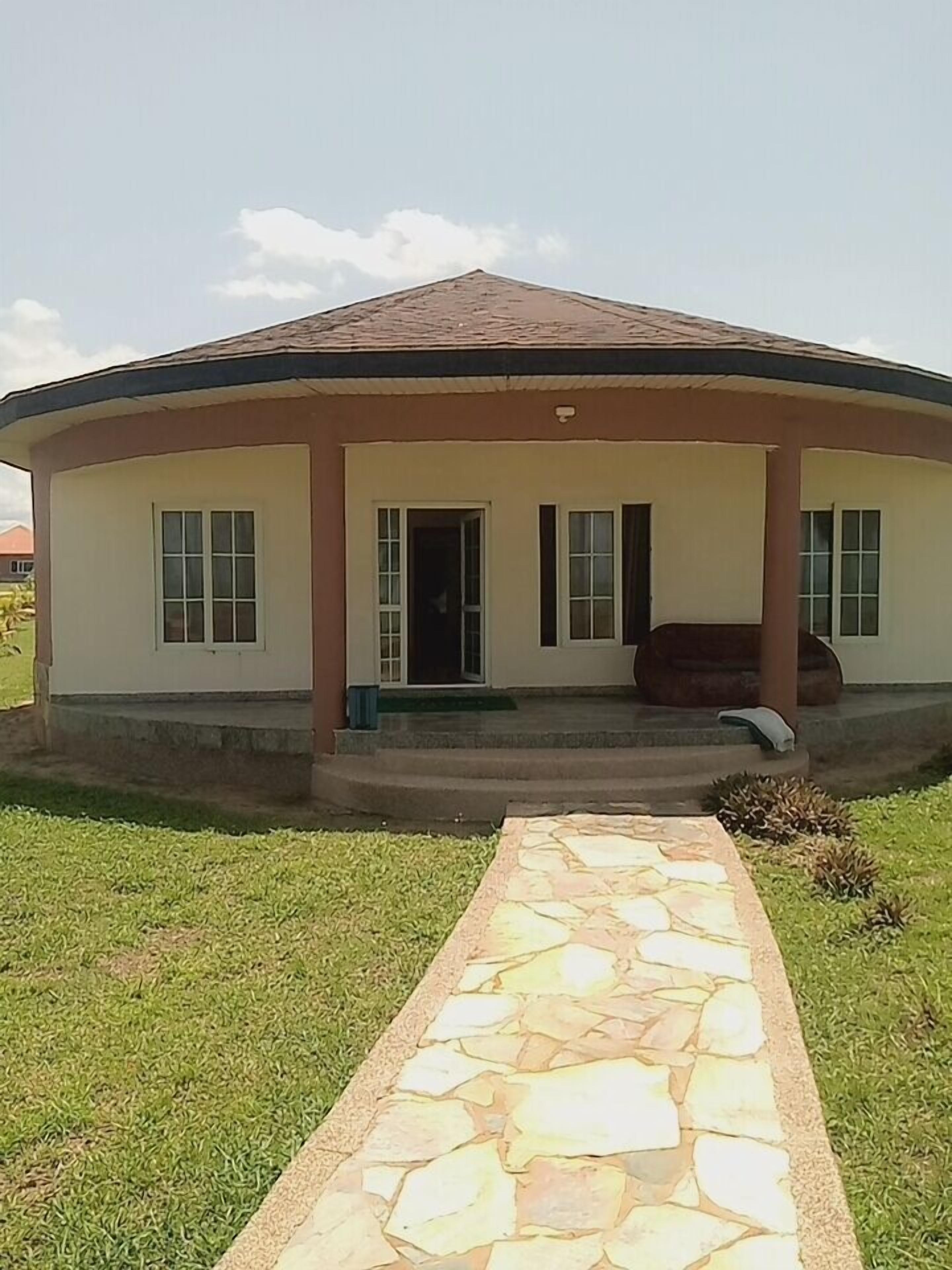 A circular building with a covered porch, a stone pathway leading to the entrance, and a grassy lawn.