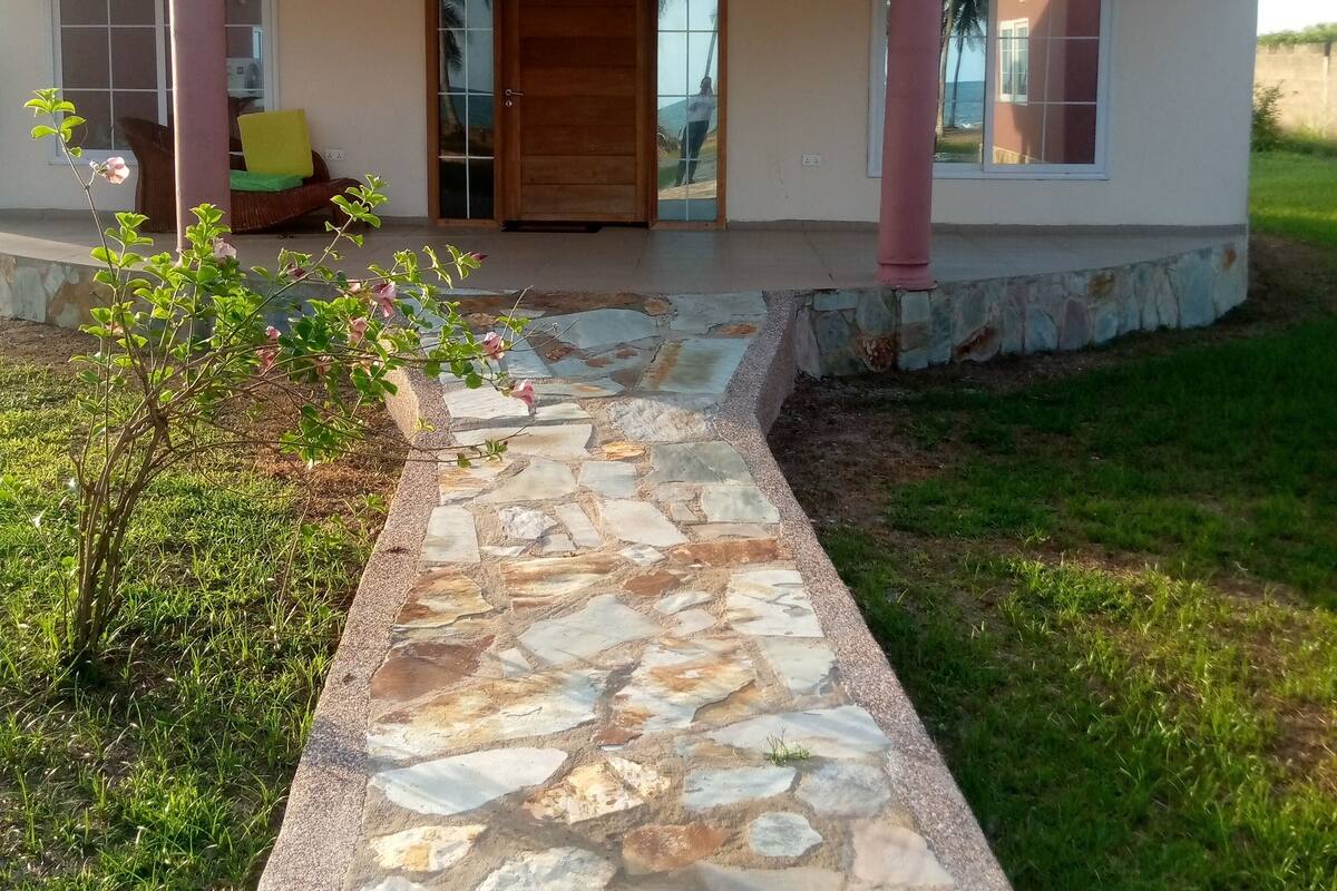 A house with a stone pathway leading to the entrance, a covered porch, and a view of the surrounding landscape.