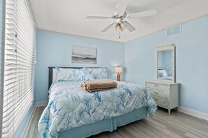 A bedroom with a bed, a ceiling fan, a dresser, and a window with blinds.