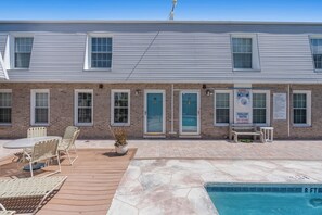 A two-story building with a brick facade, numbered doors, a pool area with a sign indicating shallow water, and outdoor seating.