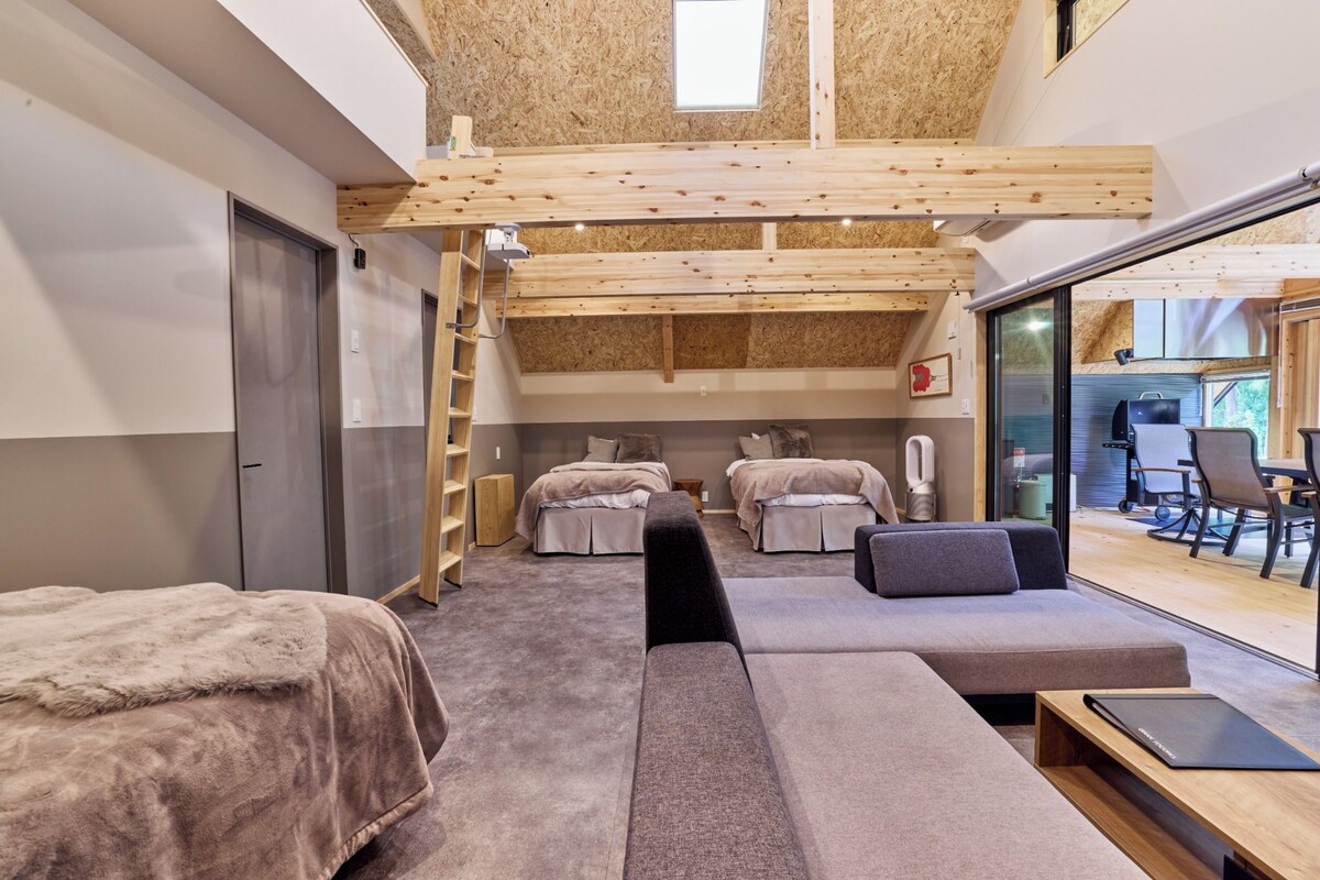 A modern room with a loft bed, a sofa, and a desk. There is a sliding glass door to the outside.