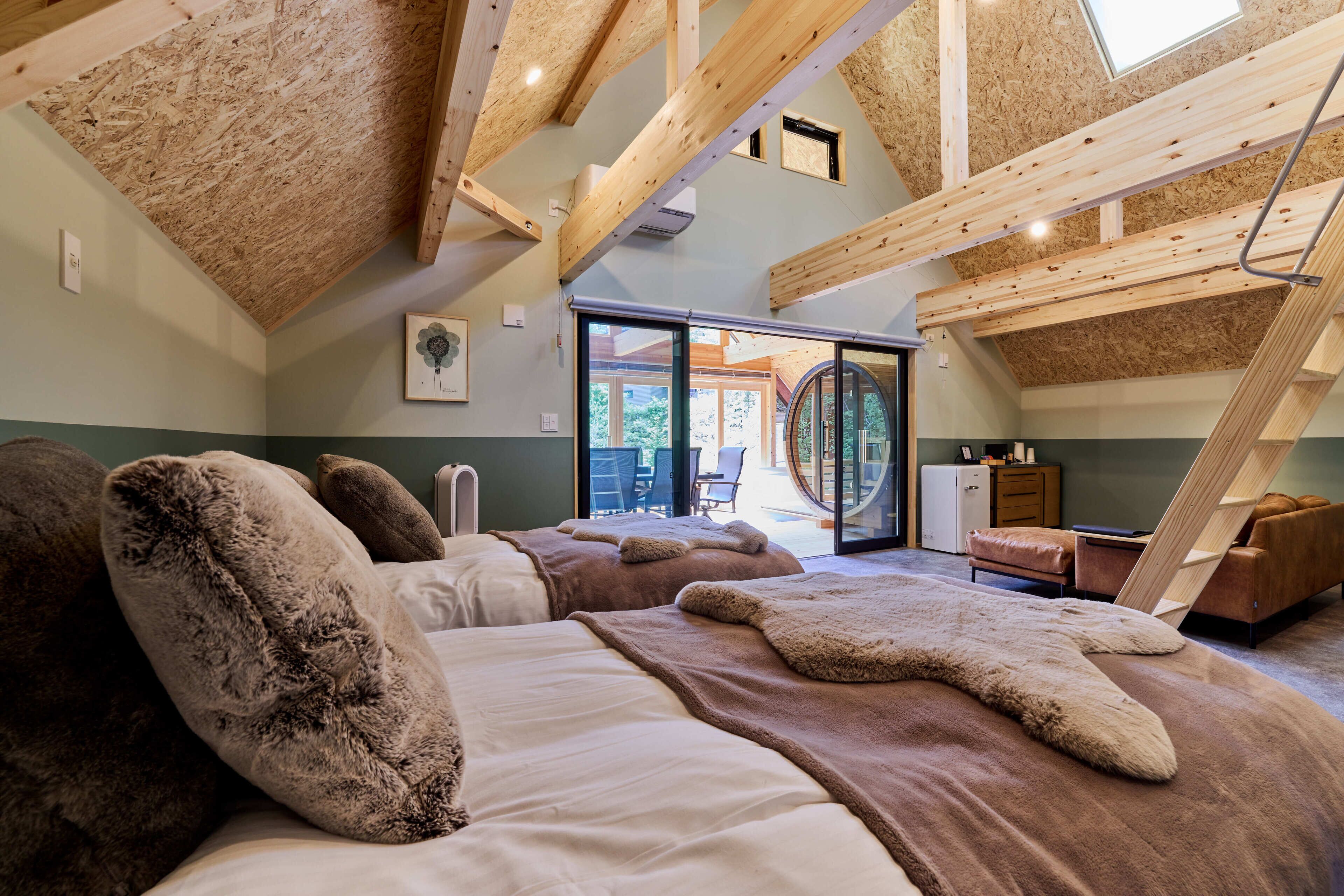 A spacious bedroom with a sloped ceiling, wooden beams, and a large bed with fluffy pillows.